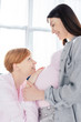 © LIGHTFIELD STUDIOS - Side view smiling woman touching belly and looking at pregnant girlfriend in pajamas in bedroom