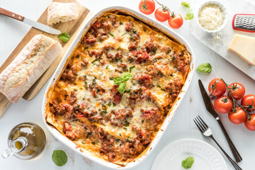 A top down view of a baked lasagna ready for serving surrounded by Italian ingredients.