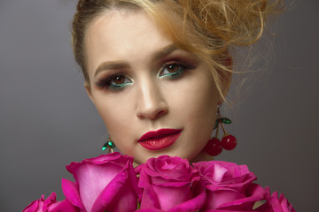 beauty portrait of a beautiful young girl. a pretty woman with brightly dressed and lips and eyes holds red-pink rose flowers. gray background. make up.