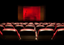 Rows Of Red Empty Chairs In Front Of Stage With Microphone On Stand
