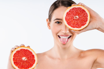 Wall Mural - Close up portrait of happy young woman holding half grapefruit close to side isolated over white background