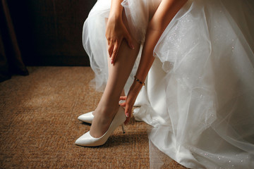 Wall Mural - The bride in a beautiful wedding dress puts on shoes, the morning of the bride, a beautiful girl waiting for the groom, gold jewelry, beautiful legs of the bride, preparation for the wedding day