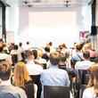 © kasto - Talk in conference hall at business event. Audience at the conference hall. Business and Entrepreneurship concept. Focus on unrecognizable people in audience. Copy space on empty white screen.