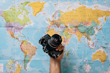 detail of a man's hand holding a photo camera with a world map in the background. Fun lifestyle concept while traveling.