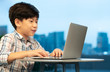 © myboys.me - Online learning, homeschooling and video call studying during Covid-19 concept. Smart looking Asian boy watch, talk and type on computer laptop in his urban condo with buildings in city in background.