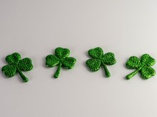 4 Green Glittery Four Leaf Clovers Lined Up On A White Background For St. Patrick’s Day.
