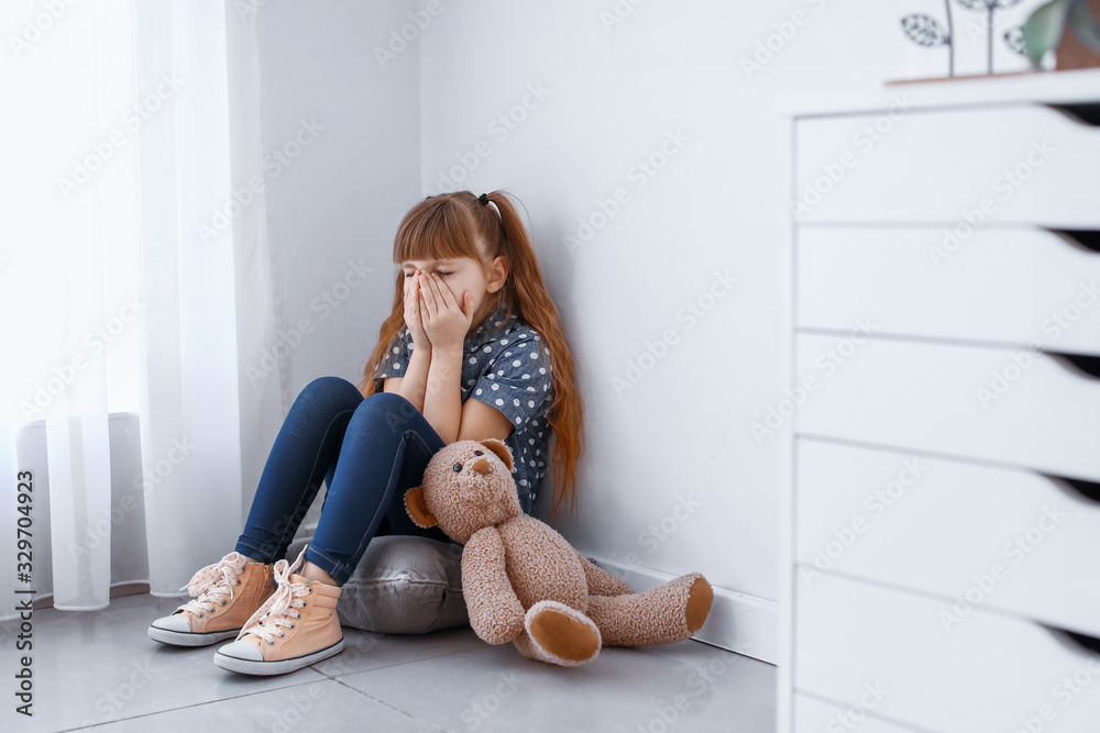 Scared little girl sitting in corner at home. Concept of violence
