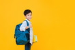 Smiling handsome mixed race schoolboy with books and backpack giving thumbs up isolated on yellow background with copy space