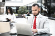 © Mangostar - Serious focused male manager working on report and using laptop in coffee shop. Young black woman using tablet in background. Wireless technology concept