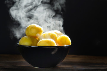 Wall Mural - Steaming of boiled hot potatoes  in a black  bowl and butter served on wooden table ready to eat. 