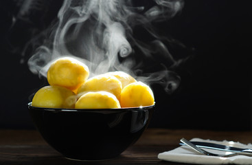 Wall Mural - steaming of boiled hot potatoes in a black bowl and butter served on wooden table ready to eat.