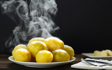 Steaming of boiled hot potatoes  in a white plate and butter served on wooden table ready to eat. 