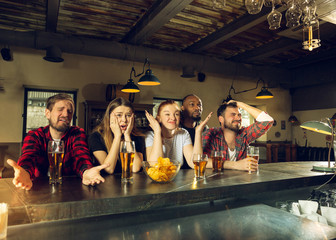 Wall Mural - Sport fans cheering at bar, pub and drinking beer while championship, competition is going. Multiethnic group of friends excited watching translation. Human emotions, expression, supporting concept.