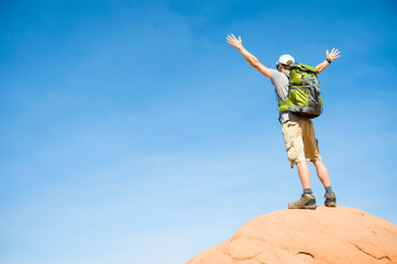 Unrecognizable hiker standing outdoors with arms raised on the top of a red rock mountain