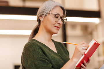 Canvas Print - Photo of concentrated mature woman making notes in diary while sitting