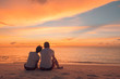 © icemanphotos - Couple in love watching sunset together on beach travel summer holidays. People silhouette from behind sitting enjoying view sunset sea on tropical destination vacation. Romantic couple on the beach