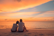 Couple In Love Watching Sunset Together On Beach Travel Summer Holidays. People Silhouette From Behind Sitting Enjoying View Sunset Sea On Tropical Destination Vacation. Romantic Couple On The Beach