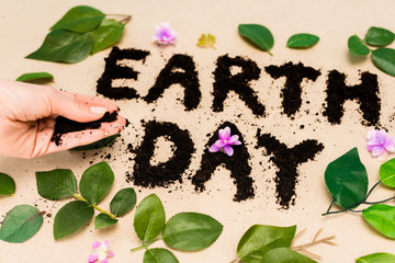 Wall Mural - Cropped view of handful of ground in female hand, earth day lettering with leaves and buds on beige