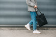 canvas print picture - Cropped photo of the bottom of a young man in stylish clothes walking on the background of a gray wall with an black eco bag in his hand. Eco friendly. Reusable bag in young man's hand. Copy space