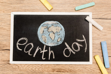 Wall Mural - Top view of black board with earth day lettering and pieces of chalk on wooden background