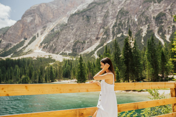 Wall Mural - Cute girl in long vintage white dress enjoy amazing fabulous nature. Backdrop alpine lake Braies, turquoise water, white mountains, green forest. Summer.