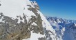 Mountains covered in show. Rocks still visible. Clear blue sky and sun in the Swiss Alps. Captured by drone.