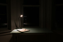 Home Desk At Night With A Light And Notebook With A Pencil