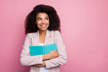 Poster - Photo of funny pretty dark skin lady hold journal book close to chest look side empty space imagination flight wear checkered blazer isolated pastel pink color background