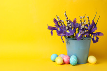 Easter Eggs And Bucket With Flowers On Yellow Background, Space For Text