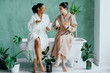 © Iryna - Cute young two women dressed in white dressing gowns and towels on the head have fun in the bathroom