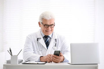 Canvas Print - Senior doctor with smartphone at table in office