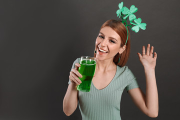 Wall Mural - Young woman with clover headband and green beer on grey background, space for text. St. Patrick's Day celebration