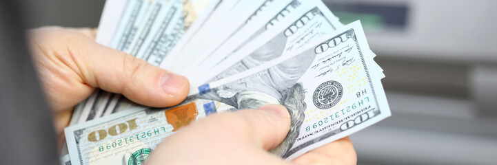 Male hands holding fantail of hundred dollars banknotes at atm machine