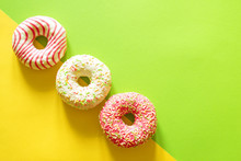 Colorful Donuts With Pink Frosting And Sprinkles On Green And Yellow Background
