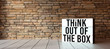 lightbox with message THINK OUTSIDE THE BOX in front of brick wall on wooden floor