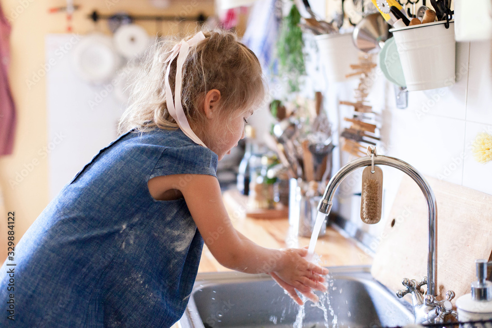 Kid washing hands at home under water tap. Cute child girl in flour after cooking in cozy home kitchen. Infection prevention. Avoid spreading viruses and germs. - obrazy, fototapety, plakaty 