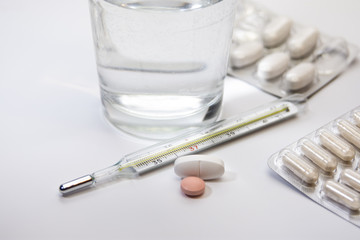 thermometer pills and tablets lying scattered on white isolated background 