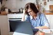 © Mary Anlens - Upset woman working from home office. Worry freelancer using laptop and the Internet. Workplace in cozy kitchen. Concept of female business and career, housekeeping, stress. Lifestyle moment.