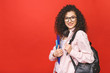 Young curly student woman wearing backpack glasses holding books and tablet over isolated red background.