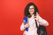 © denis_vermenko - Young curly student woman wearing backpack glasses holding books and tablet over isolated red background.  Ok sign.