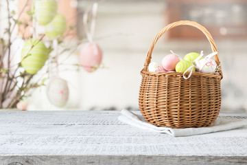 Wicker basket with easter colorful eggs on kitchen wooden table. Spring easter composition. Space for text.