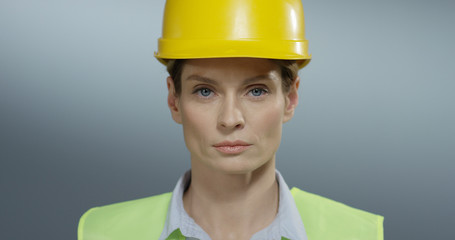 Close up of the young attractive Caucasian cheerful woman builder in the hard yellow helmet smiling to the camera. Portrait.