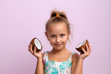 Health, natural oils, body care, cosmetology. Cheerful cheerful little girl child holds coconut halves near the face and smiles cute on an isolated light background