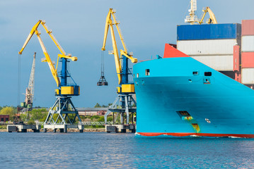 Wall Mural - Large cargo container ship leaving the port of Norfolk, close-up. Cranes in the background. Cloudy blue sky. Virginia, USA