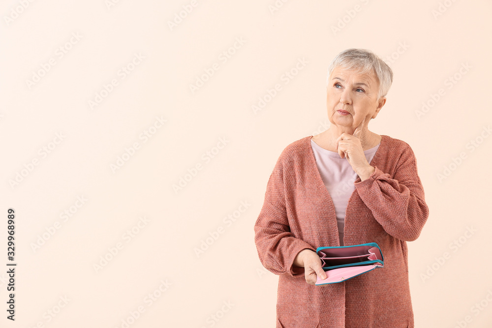 Senior woman with empty wallet on color background