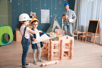 Canvas Print - Father and little children dressed as builders playing with take-apart house at home