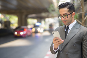 Wall Mural - Young handsome Persian businessman using phone in the city streets outdoors