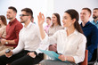 © New Africa - Young woman raising hand to ask question at business training indoors