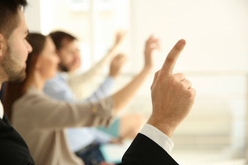 Wall Mural - Young man raising hand to ask question at business training indoors, closeup