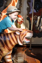 Boy Sitting On Carousel Tiger In Amusement Park